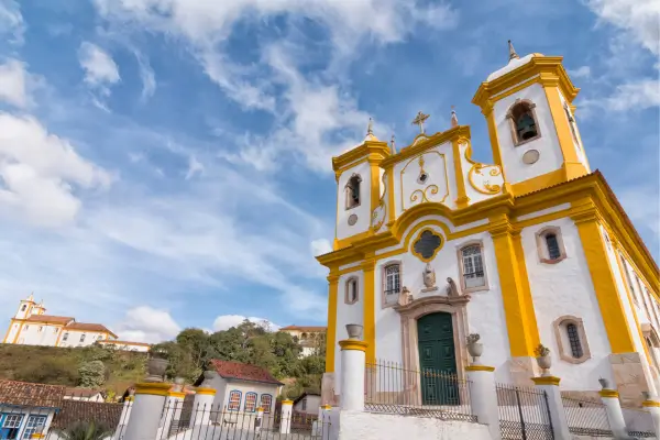 “Igreja barroca de Minas Gerais com fachada branca e amarela, destacando torres, ornamentos e arquitetura colonial sob céu azul.”