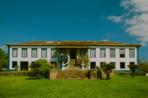 “Fazenda centenária de arquitetura rural mineira com casarão colonial branco, janelas azuis e jardim gramado”