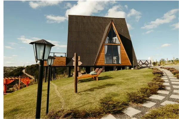 “Cabana em estilo A-frame em área rural de Minas Gerais, com gramado, vista para as montanhas e estrutura de hospedagem integrada à natureza.”