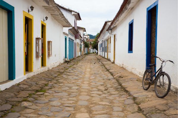 “Casas coloniais alinhadas em rua de pedra com bicicleta encostada, representando cidades históricas de Minas.”