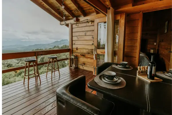 “Varanda e interior de cabana de madeira com vista para as montanhas de Minas Gerais, oferecendo hospedagem aconchegante em meio à natureza.”