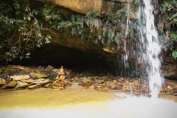 “Pequena queda d’água escorrendo de formação rochosa com vegetação, em gruta natural de São Tomé das Letras, MG.”