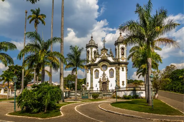 "Igreja barroca de São João del Rei (MG) cercada por palmeiras imperiais em um dia ensolarado"