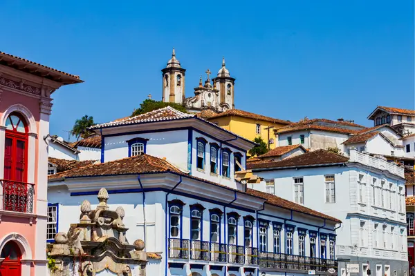 “Casarões coloniais de Ouro Preto, MG, com fachadas coloridas e igreja ao fundo, representando a arquitetura histórica mineira.”