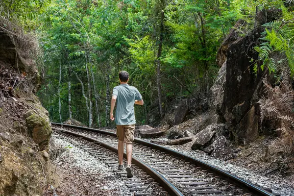 "Viajante caminhando sobre trilhos de trem entre mata fechada em antiga ferrovia histórica de Minas Gerais"