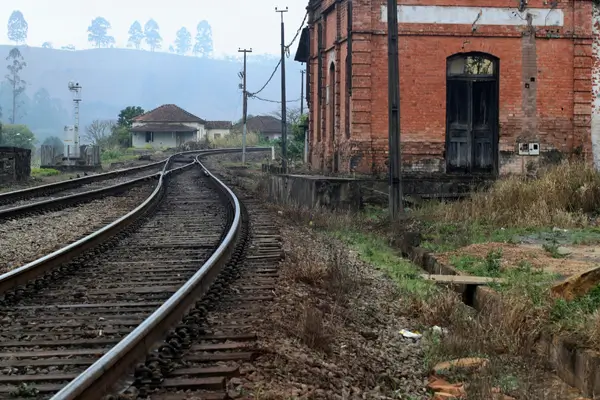 “Antiga estação ferroviária com trilhos curvos e prédio histórico de tijolos, cenário típico de hospedagens ferroviárias transformadas em charme em Minas Gerais.”