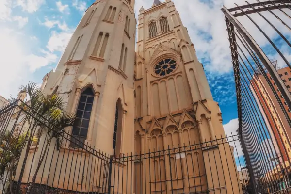 “Catedral de Montes Claros vista em ângulo baixo, destacando sua arquitetura neogótica contra o céu azul.”