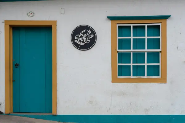 “Fachada simples de casa histórica em Sabará, Minas Gerais, com portas e janelas coloridas no estilo colonial.”