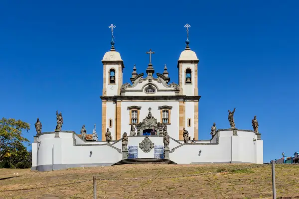 “Santuário do Bom Jesus de Matosinhos em Congonhas, com as esculturas dos Profetas de Aleijadinho diante da igreja sob céu azul.”