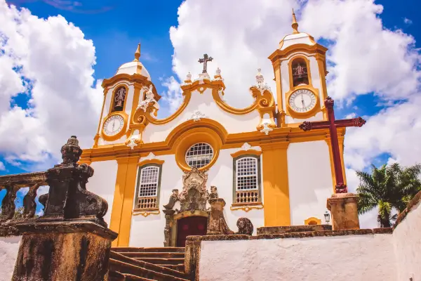 “Fachada da Matriz de Santo Antônio em Tiradentes, Minas Gerais, igreja barroca com detalhes dourados, torres ornamentadas e céu azul ao fundo.”
